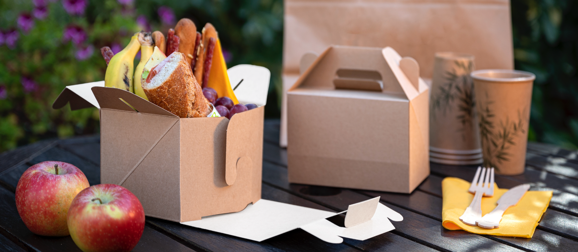 Tavolo da picnic con scatole e contenitori in cartone kraft THEPACK con panini e frutta